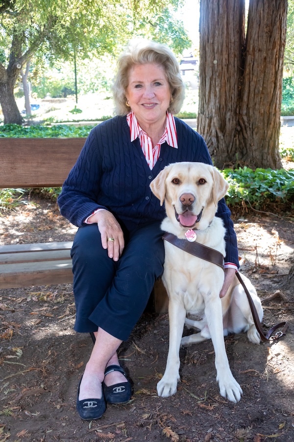 Woman seated on a bench beside her yellow Lab guide dog.