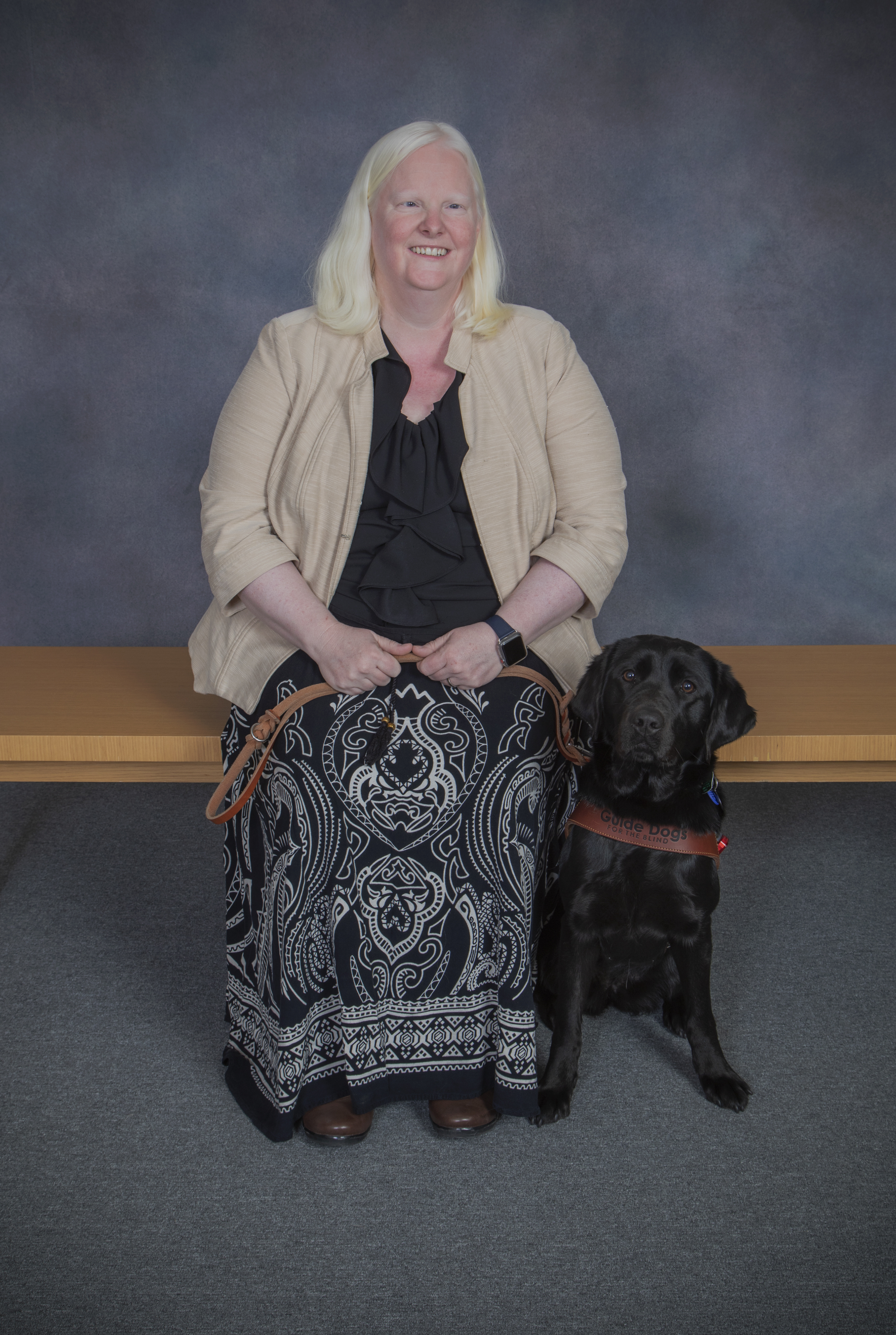 A woman seated next to a black Lab guide Dog.