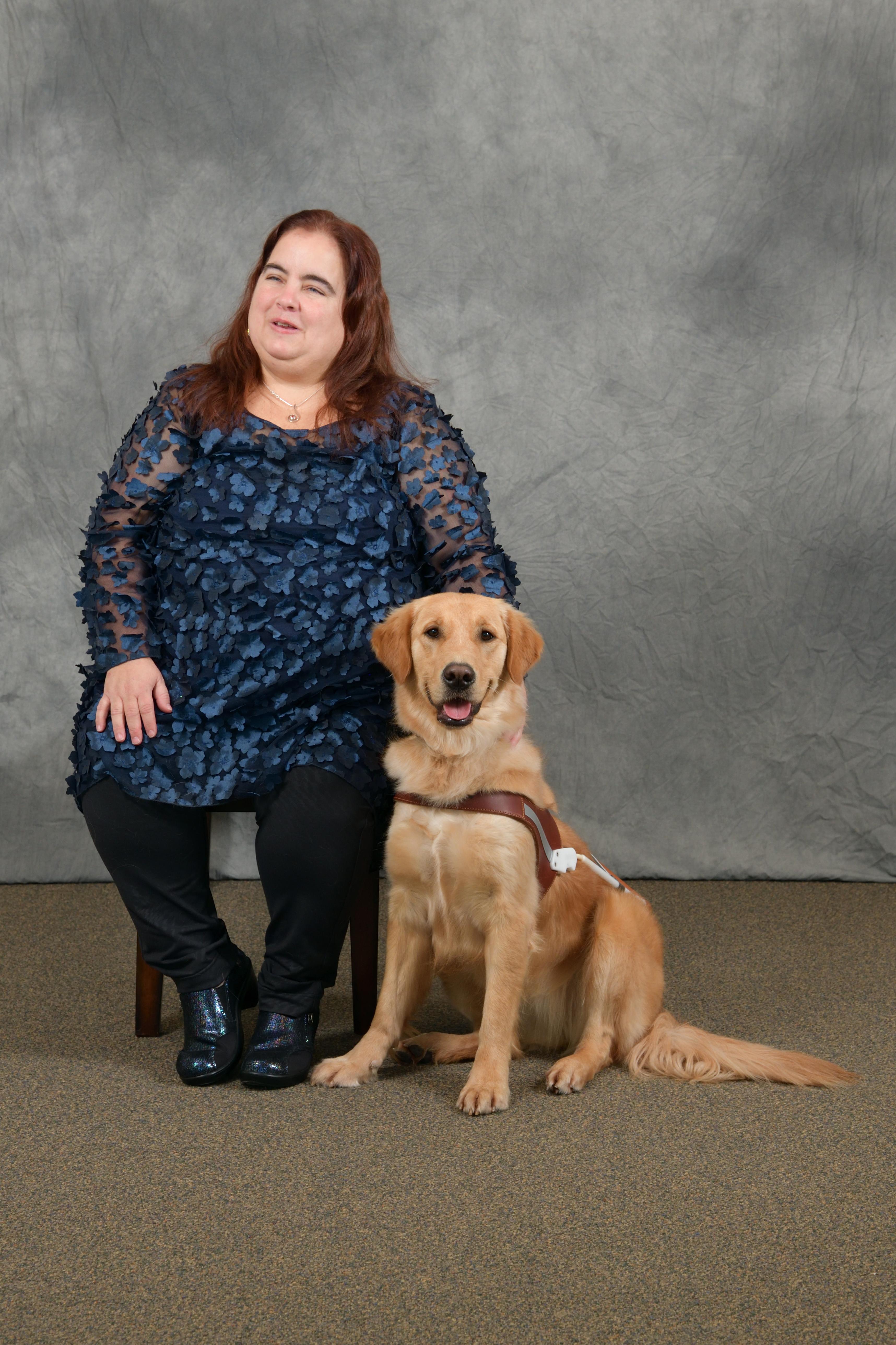Maia is seated beside her Golden Retriever guide dog, Gleam in their formal class photo.
