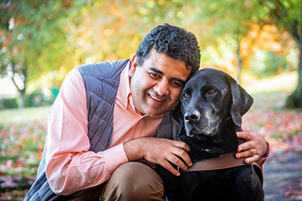 Amit Ahuja hugs his black Lab guide dog, Tashi.