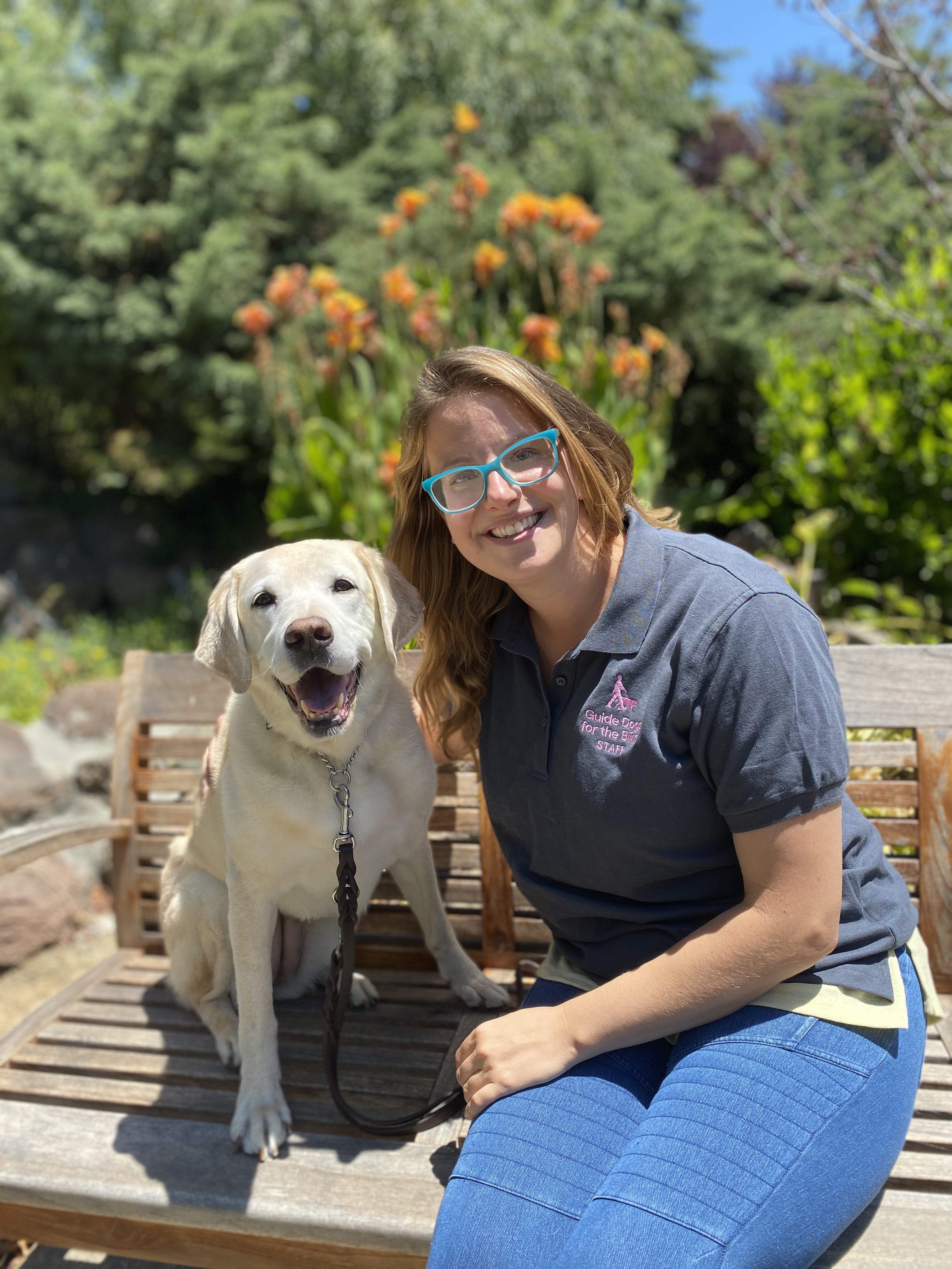 Angela sits on a bench beside a yellow Lab on a sunny day on the California campus of GDB