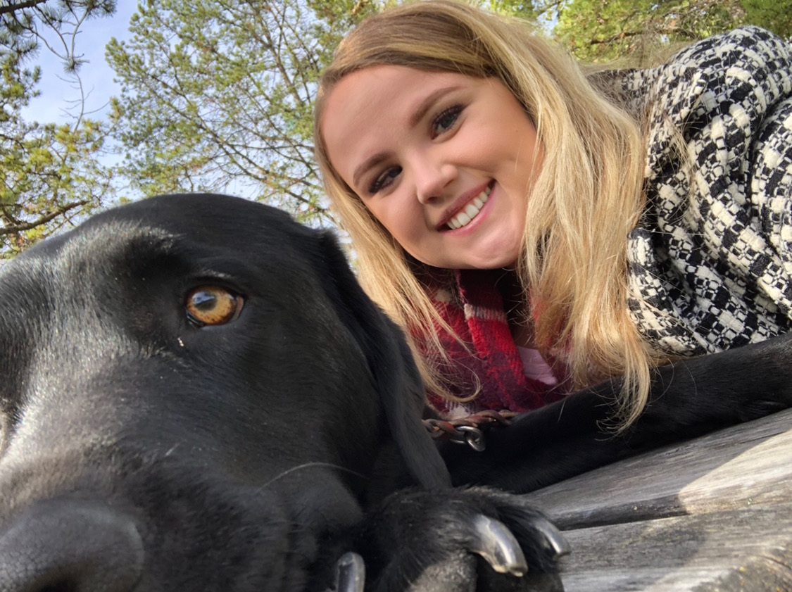 Selfie shot of Beth Deer smiling into the camera with her black Lab guide dog, Patronus, by her side.