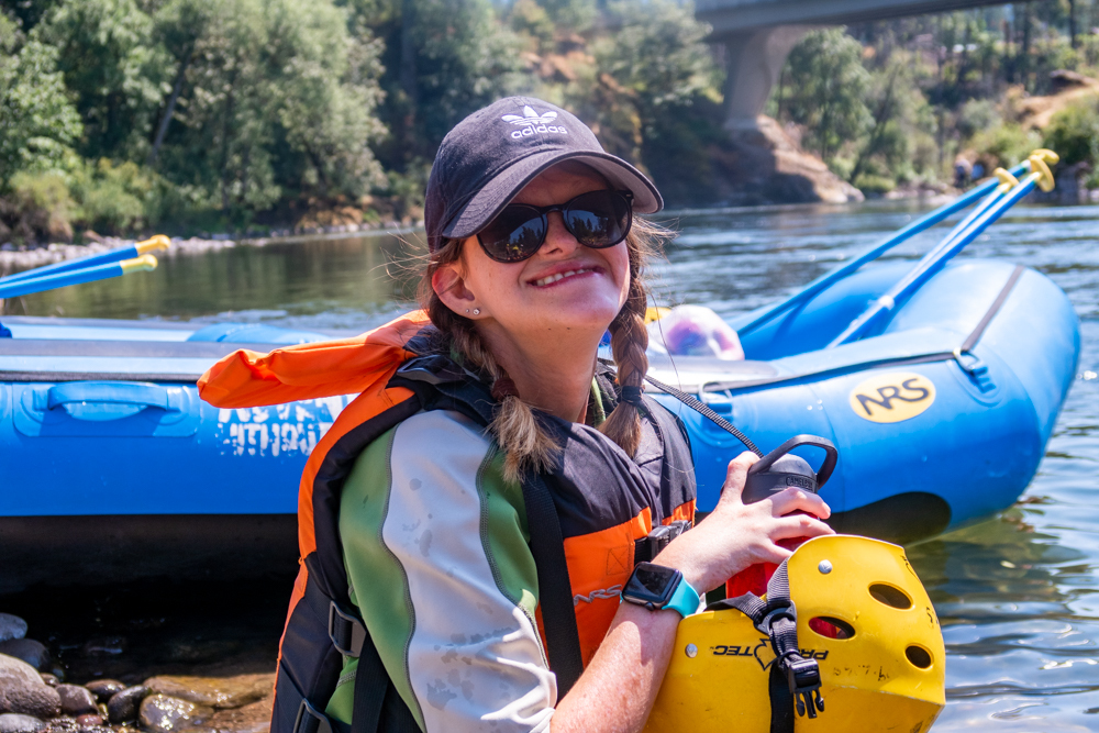 A smiling teen in front of a whitewater raft on a river.
