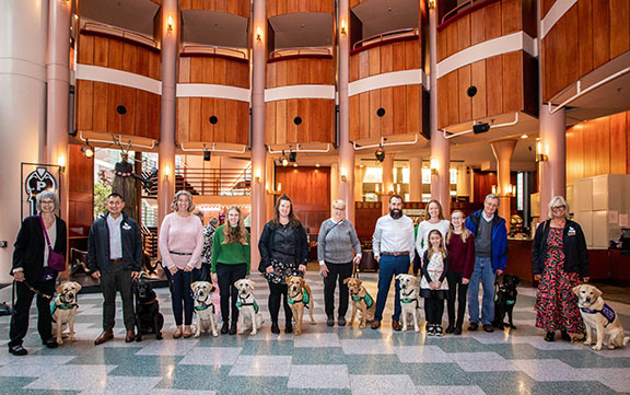Group photo of GDB puppy raising volunteers with guide dog puppies in training in a theater rotunda.