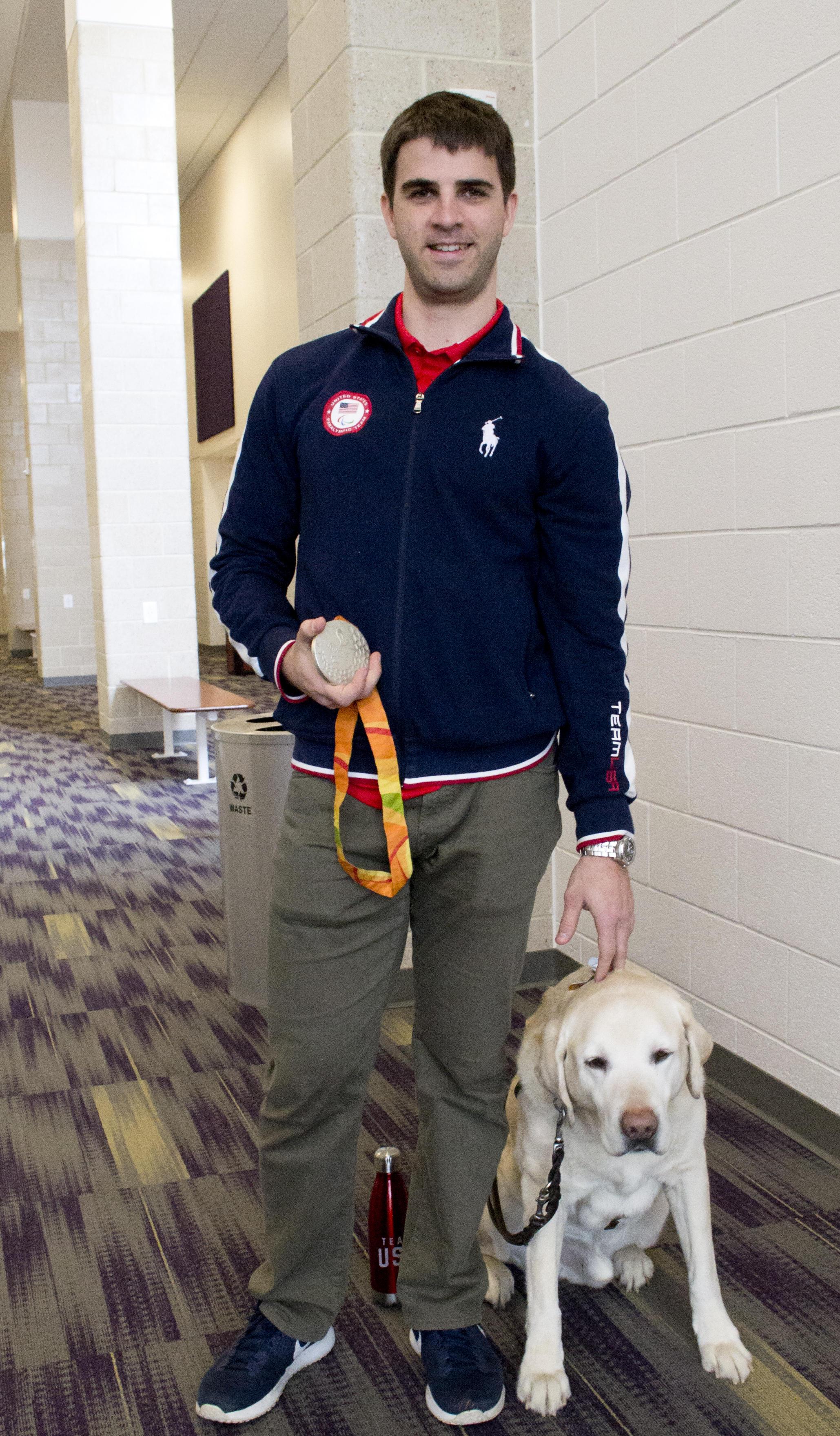 Paralympian Matt Simpson poses with his silver medal and his yellow Lab guide dog, Lacrosse.