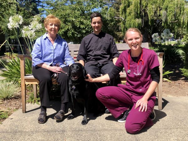 Three people and a black Lab retired guide dog.
