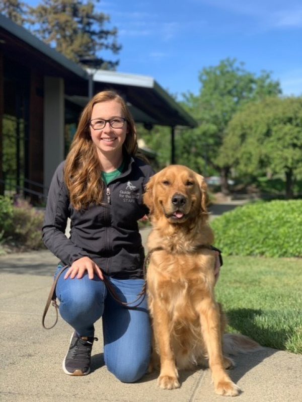 Emily Crisp kneeling next to a Golden Retriever guide dog
