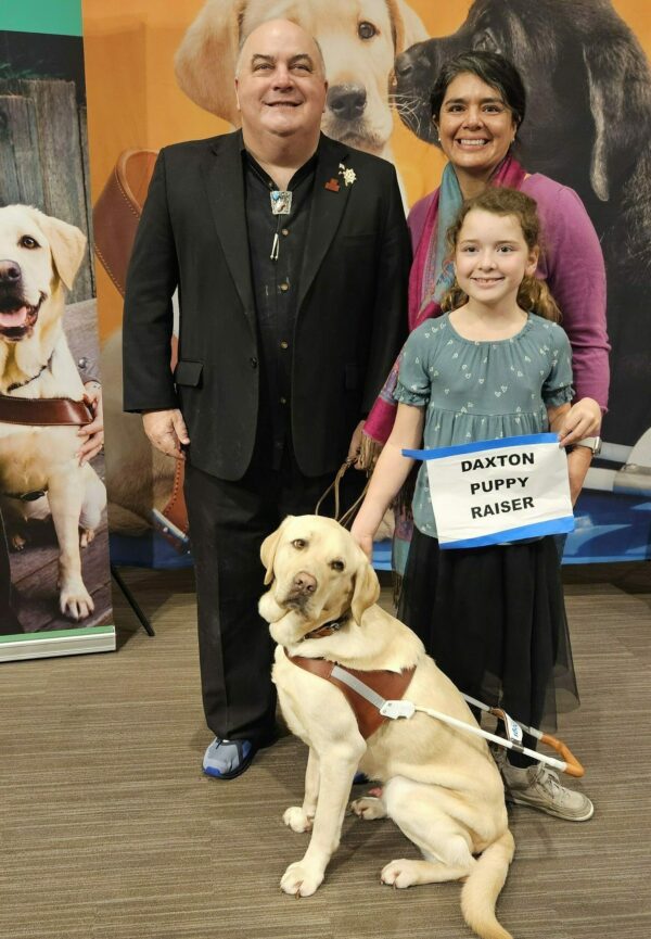 A man and his guide dog pose with a woman and her daughter.