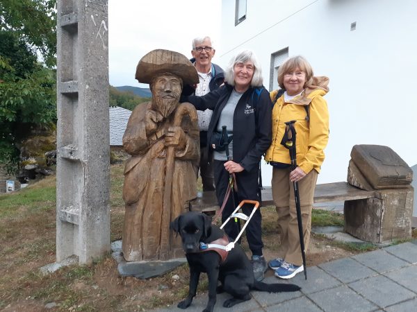 Joan and her black Lab guide dog with two friends stand next to a wooden statue of St. James on the Camino