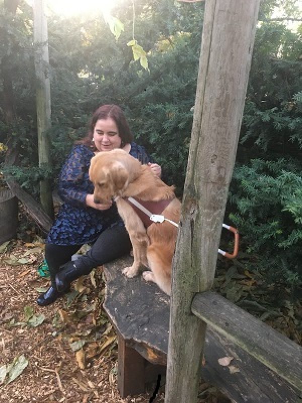 Maia Scott and her guide dog Gleam sit on a bench in the woods