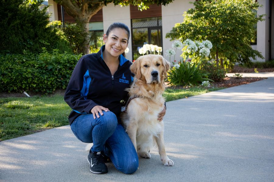 A portrait of Lauren kneeling on a sidewalk next to a Golden Retriever guide dog.