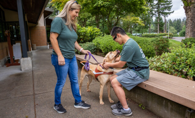 A teen boy gets an introduction to a guide dog from a guide dog mobility instructor.