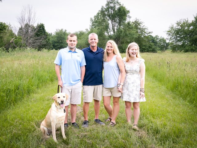 Family photo of the Edwards family including GDB clients Ethan and Elyssa. Ethan's yellow Lab guide dog, Ginsburg, stands by his side.