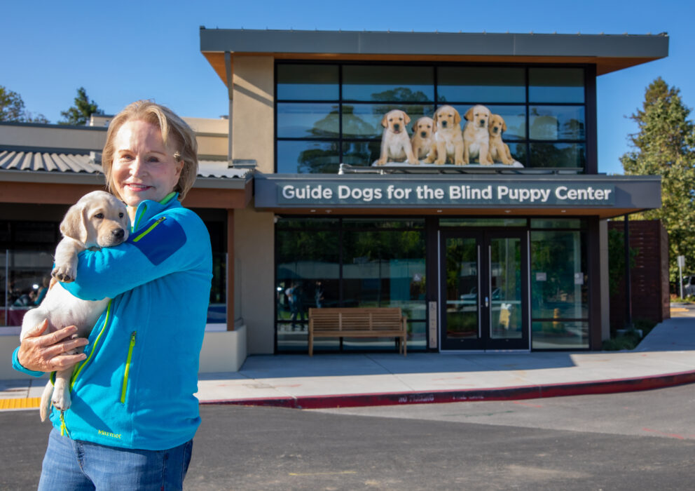 GDB CEO Christine Benninger snuggles a yellow Lab puppy in front of the Puppy Center.