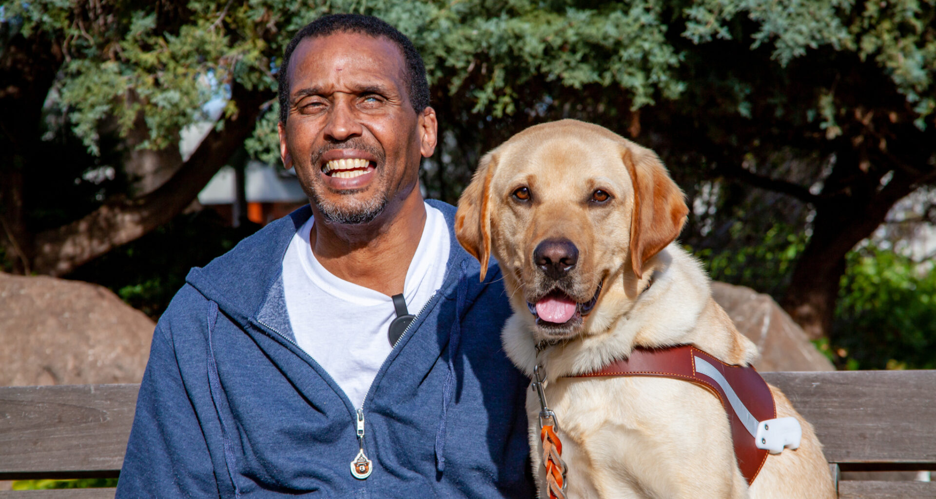 A smiling man sits next to a smiling guide dog.