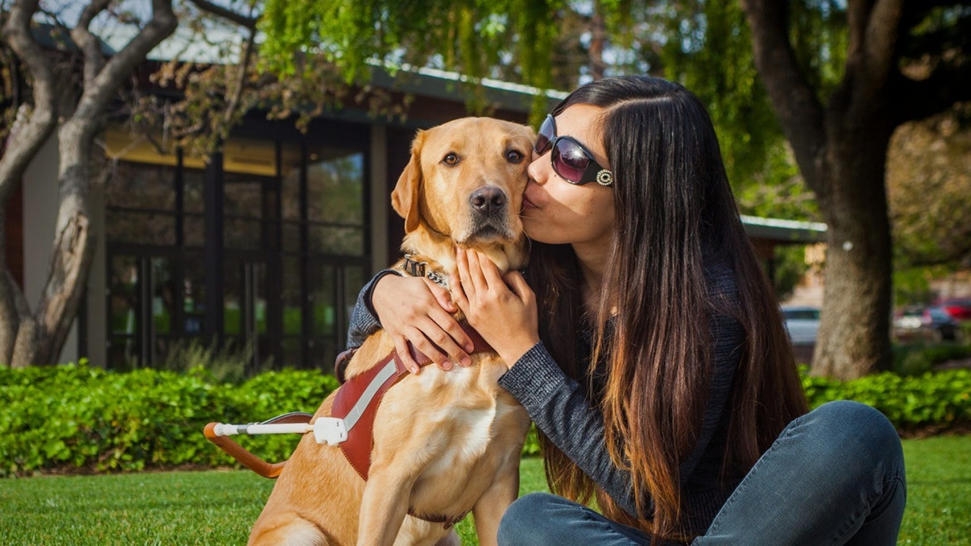A young woman kisses her yellow Lab guide dog