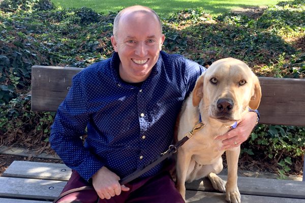 GSB staff member Scott Metzger seated on a bench next to a yellow Lab.