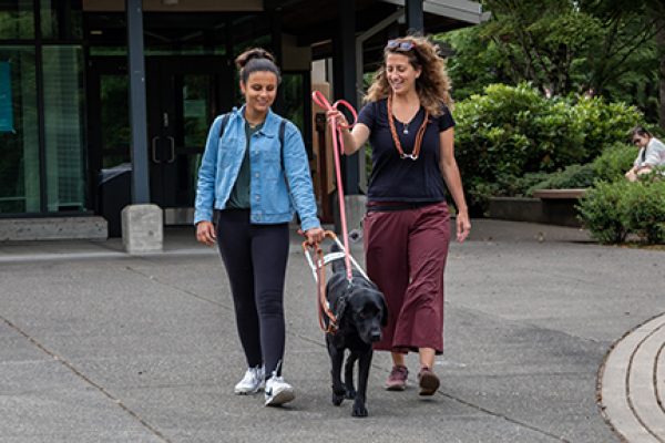 Camper Mina Lamarra walks with a black Lab guide dog alongside Guide Dog Mobility Instructor Megan Dodder