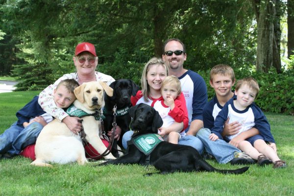 Tawna Crispin (center) with her mother, her husband and four of their children, and three guide dog puppies, from 2008.