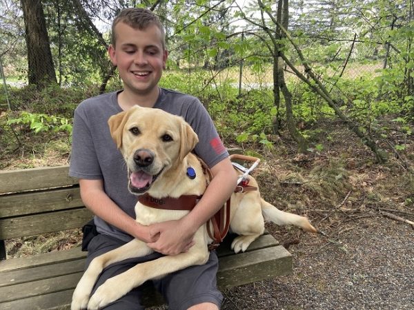 Ethan sits on a bench hugging his yellow Lab guide dog Ginsburg